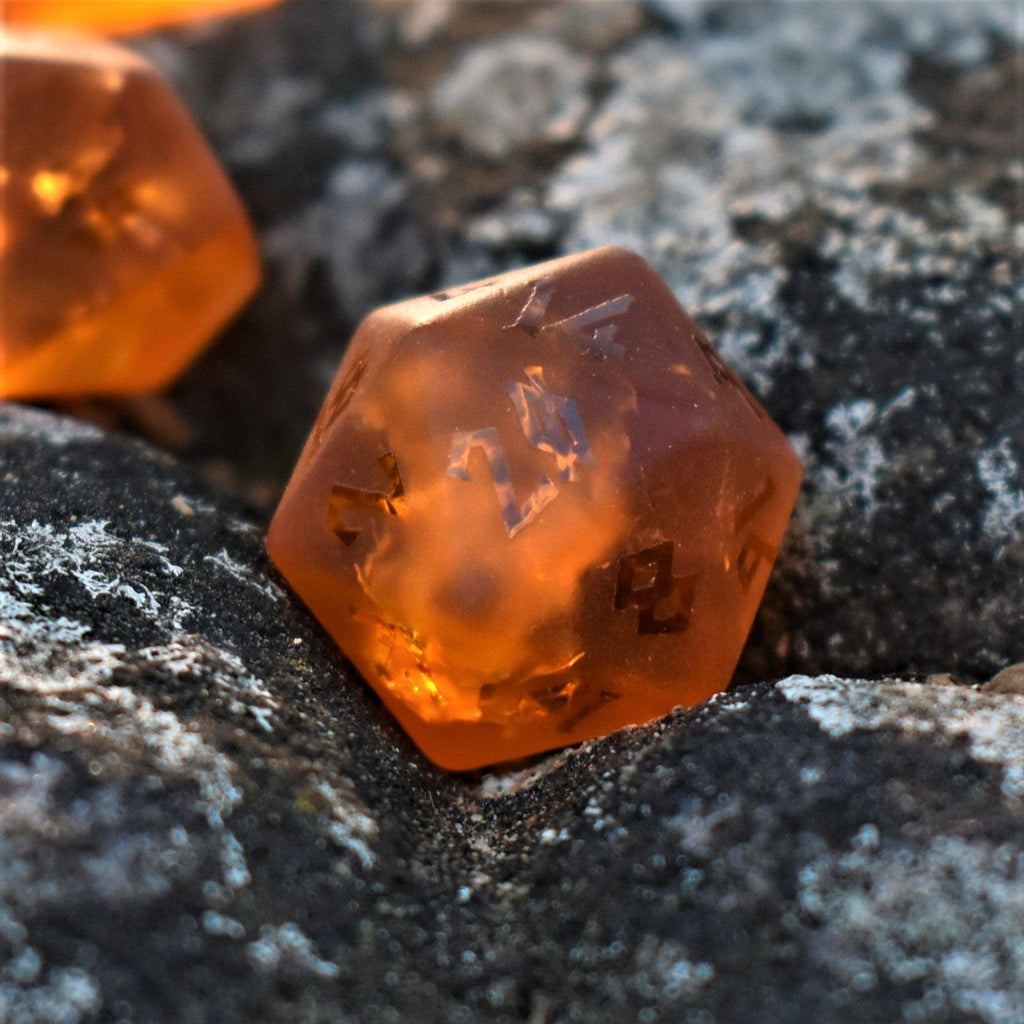 A close-up of orange glass dice with engraved numbers, resting on a rocky surface.