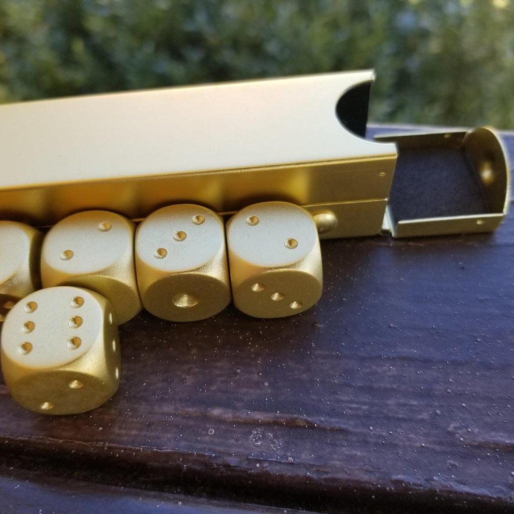 A set of gold-colored aluminum D6 dice displayed next to their foam-lined case on a wooden surface.