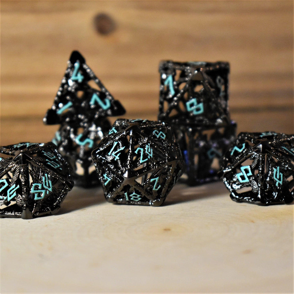 A set of hollow metal dice in black with blue embossed numbers, including various shapes such as a d4, d6, d8, d10, d12, and d20, displayed on a wooden surface.