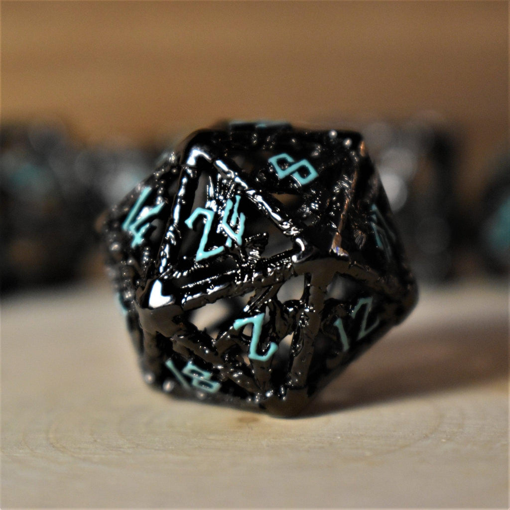 A set of hollow metal dice in black with blue embossed numbers, including various shapes such as a d4, d6, d8, d10, d12, and d20, displayed on a wooden surface.