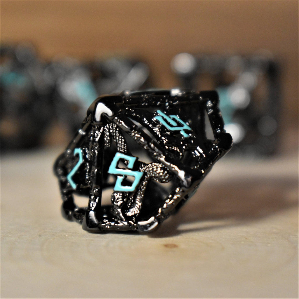 A set of hollow metal dice in black with blue embossed numbers, including various shapes such as a d4, d6, d8, d10, d12, and d20, displayed on a wooden surface.