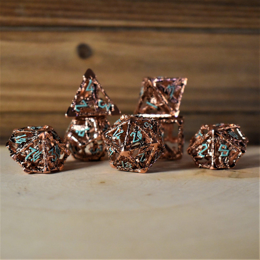 A set of copper-plated metal hollow dice with embossed numbers, including various shapes such as a D4, D6, D8, D10, D12, and D20, displayed on a wooden surface.