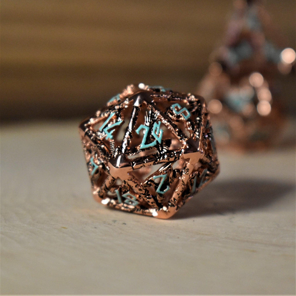 A set of copper-plated metal hollow dice with embossed numbers, including various shapes such as a D4, D6, D8, D10, D12, and D20, displayed on a wooden surface.
