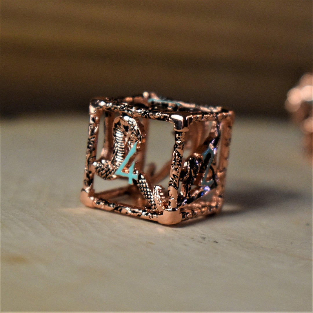 A set of copper-plated metal hollow dice with embossed numbers, including various shapes such as a D4, D6, D8, D10, D12, and D20, displayed on a wooden surface.