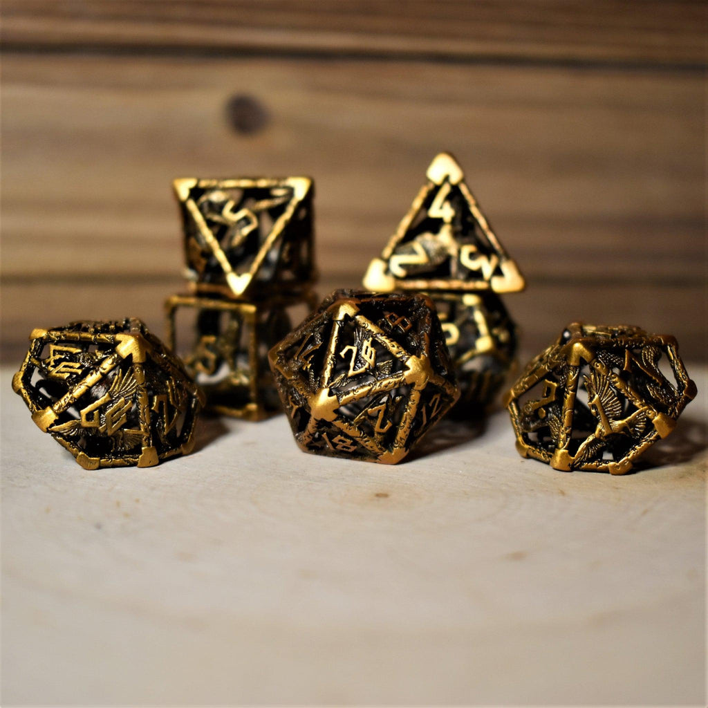 A set of golden brass hollow metal dice with embossed numbers, displayed on a wooden surface.