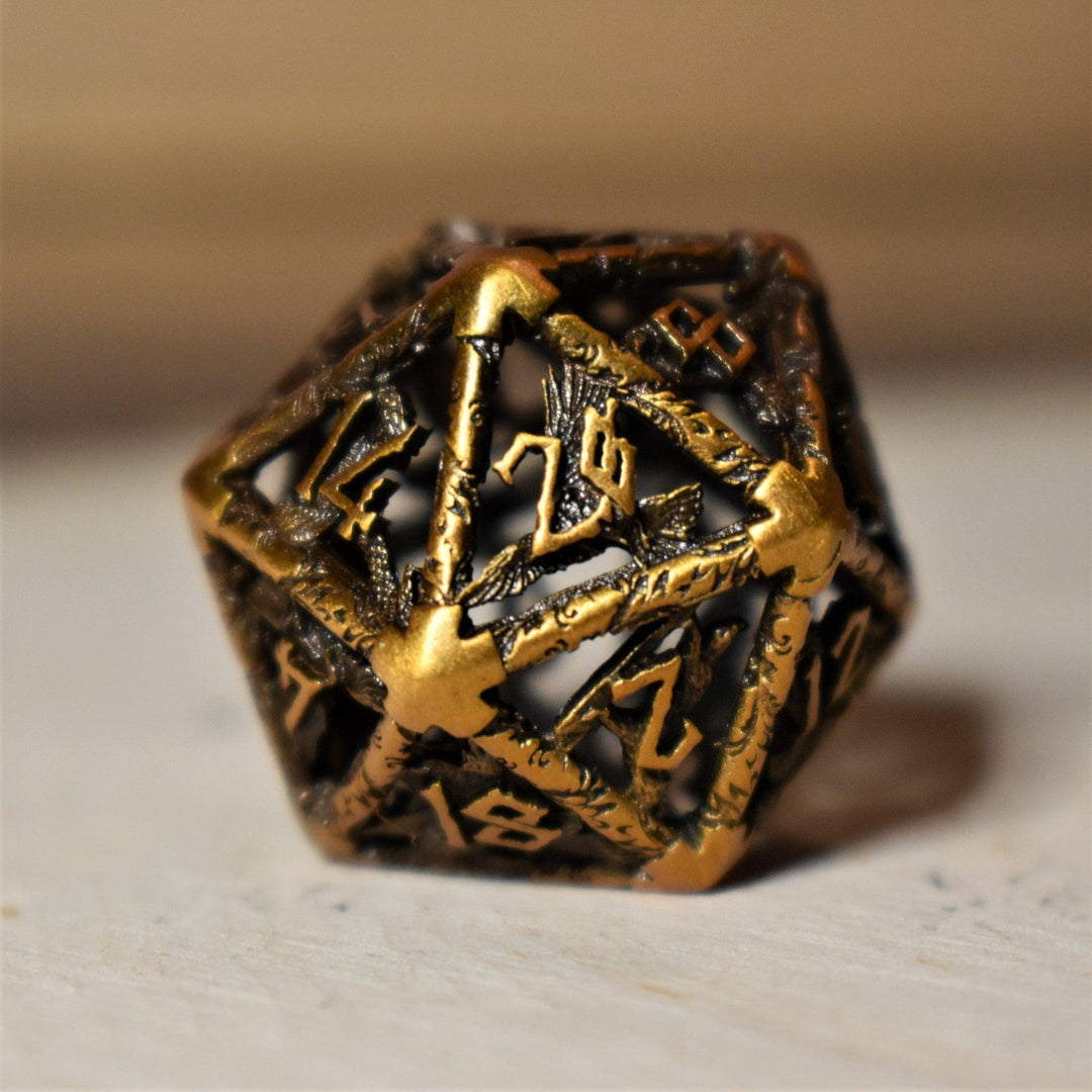 A set of golden brass hollow metal dice with embossed numbers, displayed on a wooden surface.