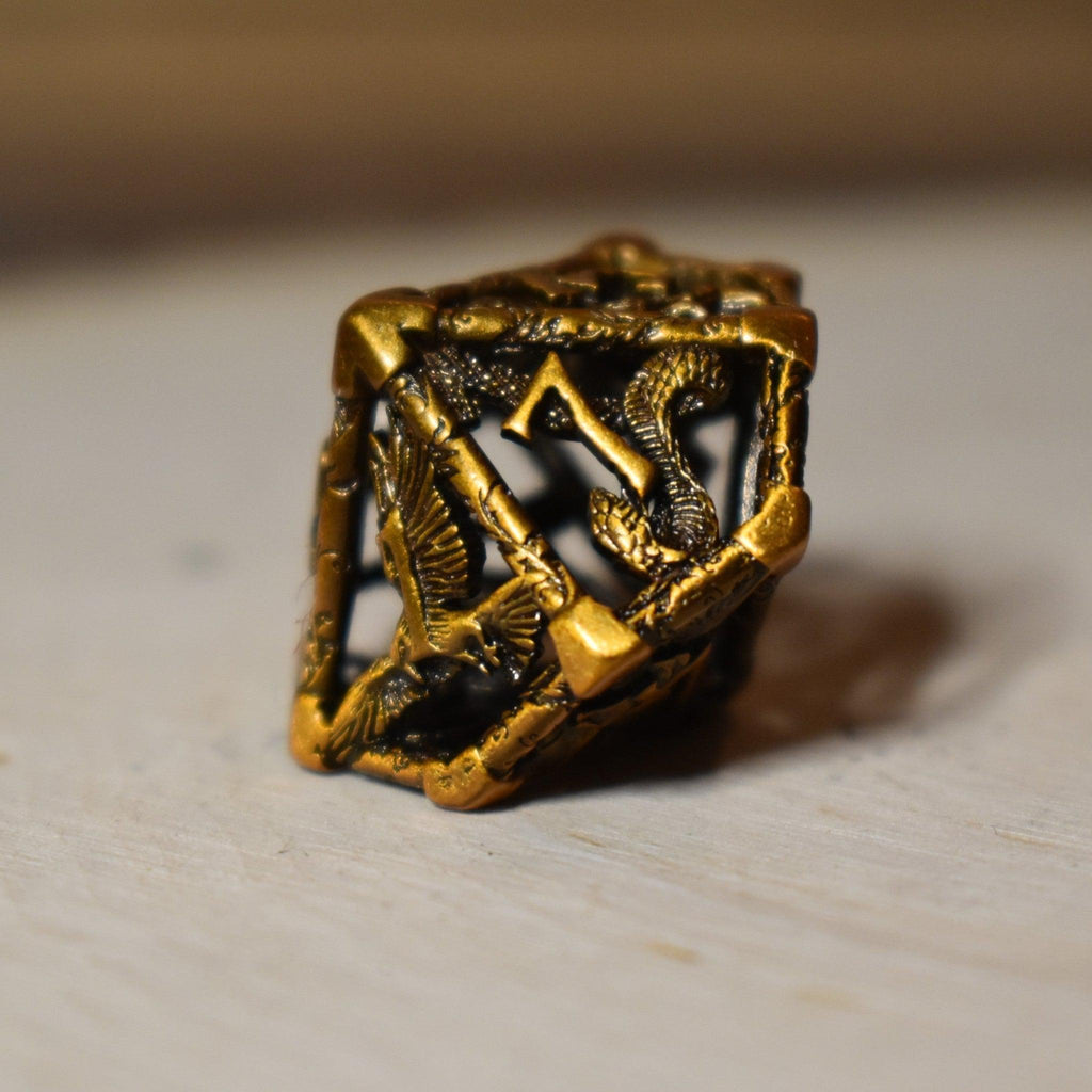 A set of golden brass hollow metal dice with embossed numbers, displayed on a wooden surface.