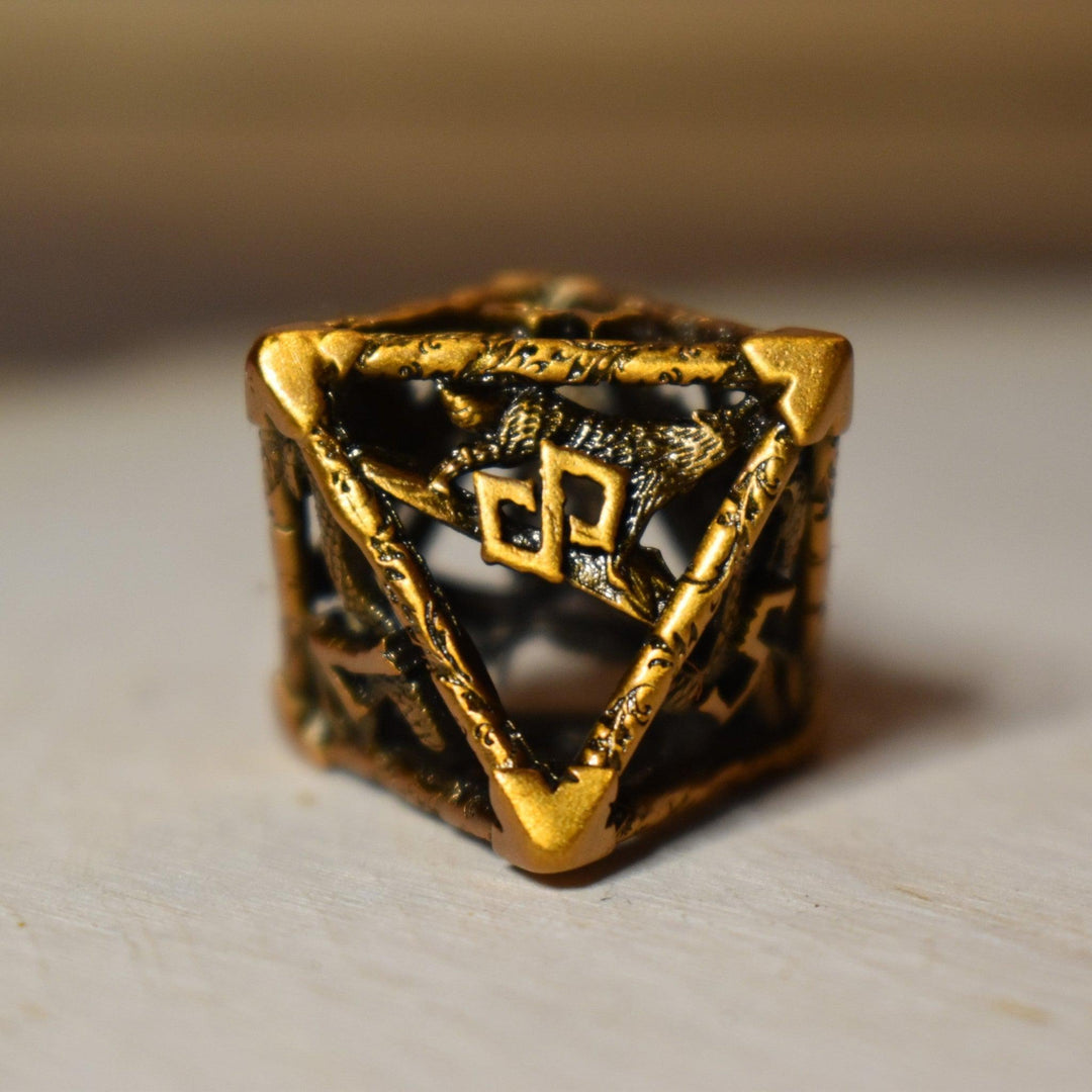 A set of golden brass hollow metal dice with embossed numbers, displayed on a wooden surface.