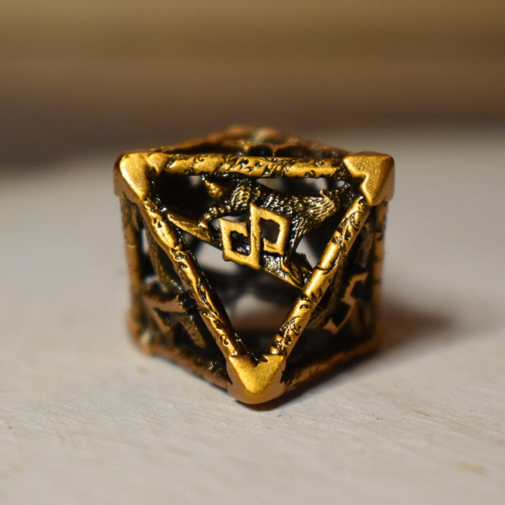 A set of golden brass hollow metal dice with embossed numbers, displayed on a wooden surface.