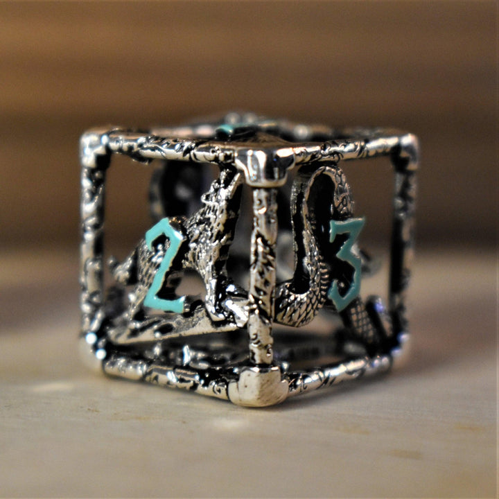 A set of silver and blue hollow metal dice with embossed numbers, displayed on a wooden surface.