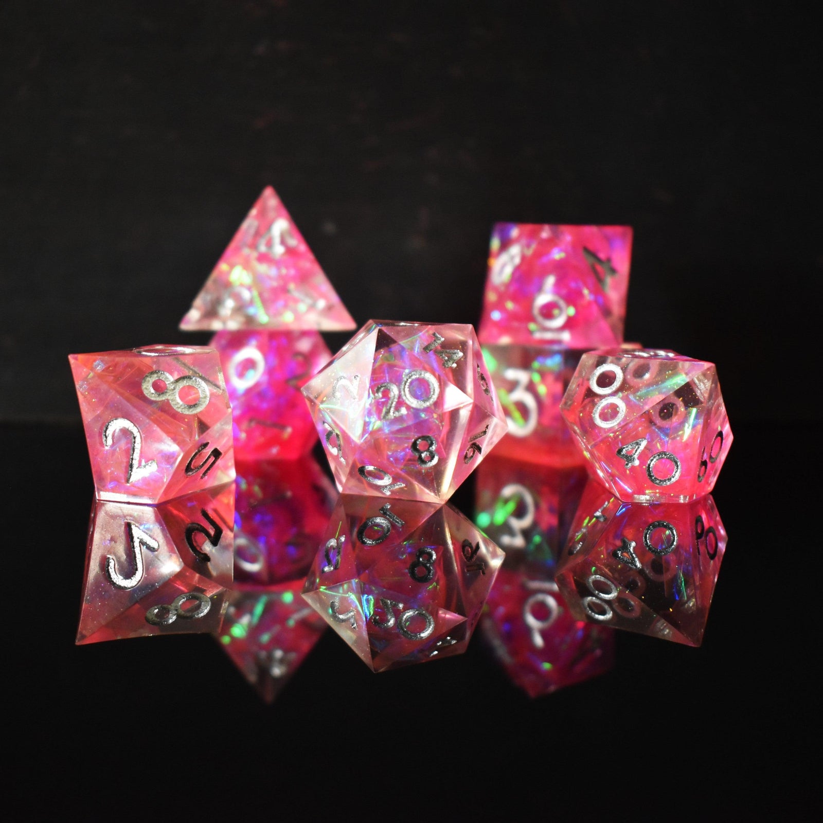 A set of sharp-edged, pink resin dnd dice with silver engraved numbers, reflecting a metallic sheen inside of each die