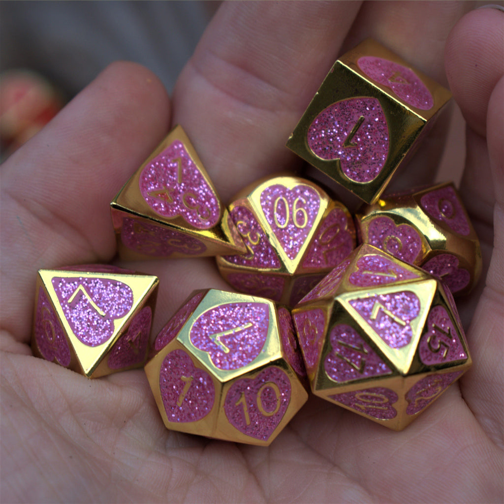 A set of gold metal dnd dice with glittery pink hearts on each face and gold numbering 