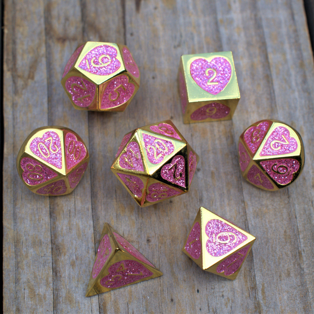 A set of gold metal dnd dice with glittery pink hearts on each face and gold numbering 