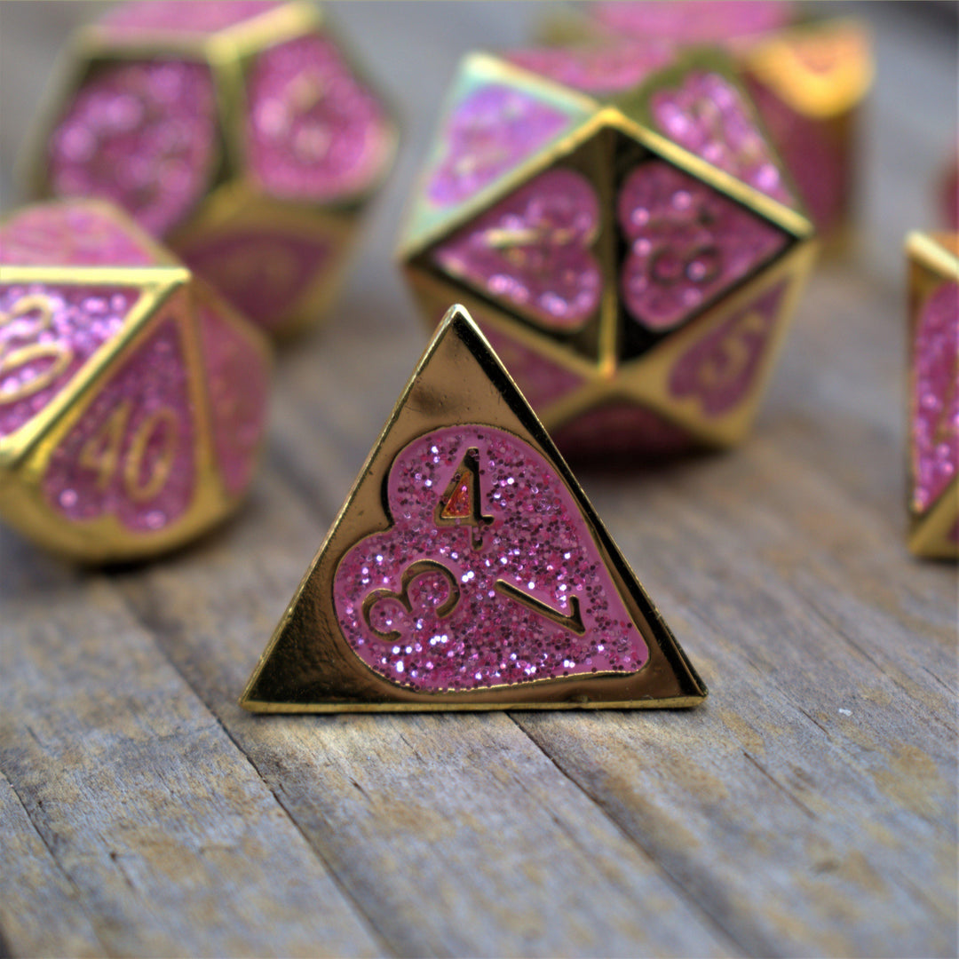 A set of gold metal dnd dice with glittery pink hearts on each face and gold numbering 