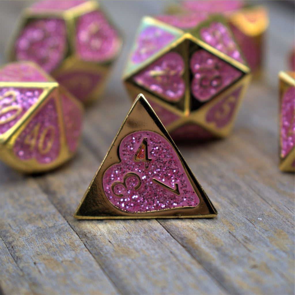 A set of gold metal dnd dice with glittery pink hearts on each face and gold numbering 
