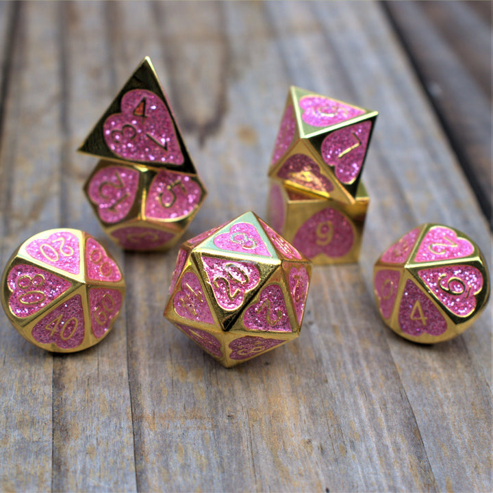 A set of gold metal dnd dice with glittery pink hearts on each face and gold numbering 