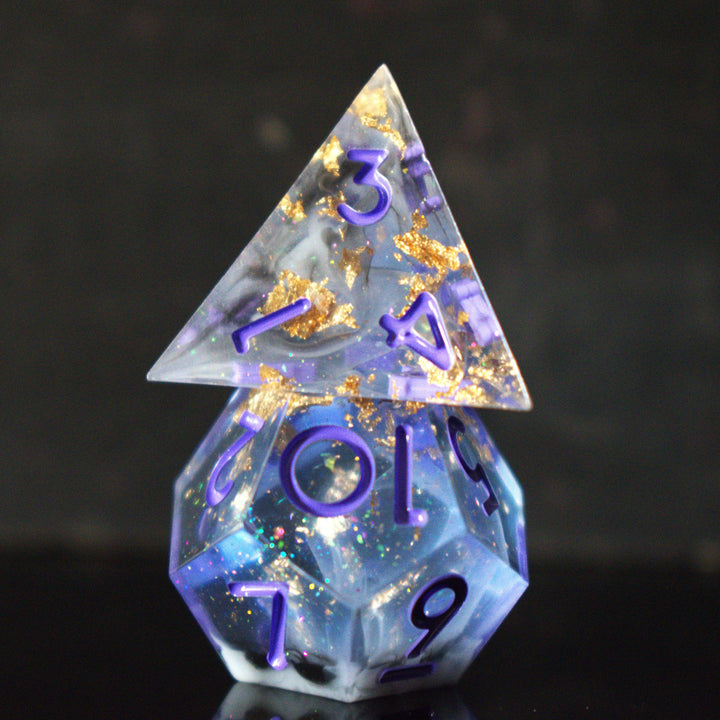 A clear, glittery sharp edge resin dnd dice set with cloudy white, gold and black running through them and purple numbering for tabletop gaming