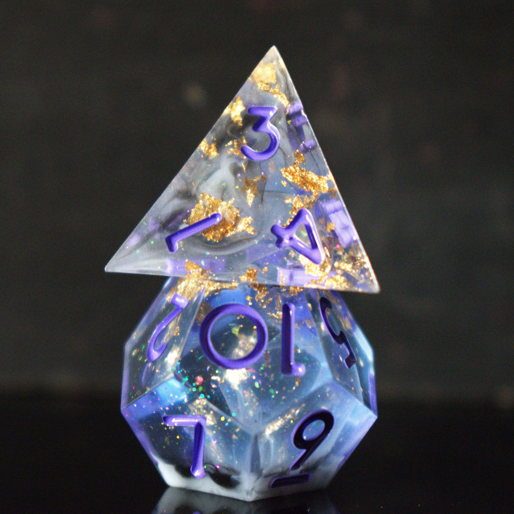 A clear, glittery sharp edge resin dnd dice set with cloudy white, gold and black running through them and purple numbering for tabletop gaming