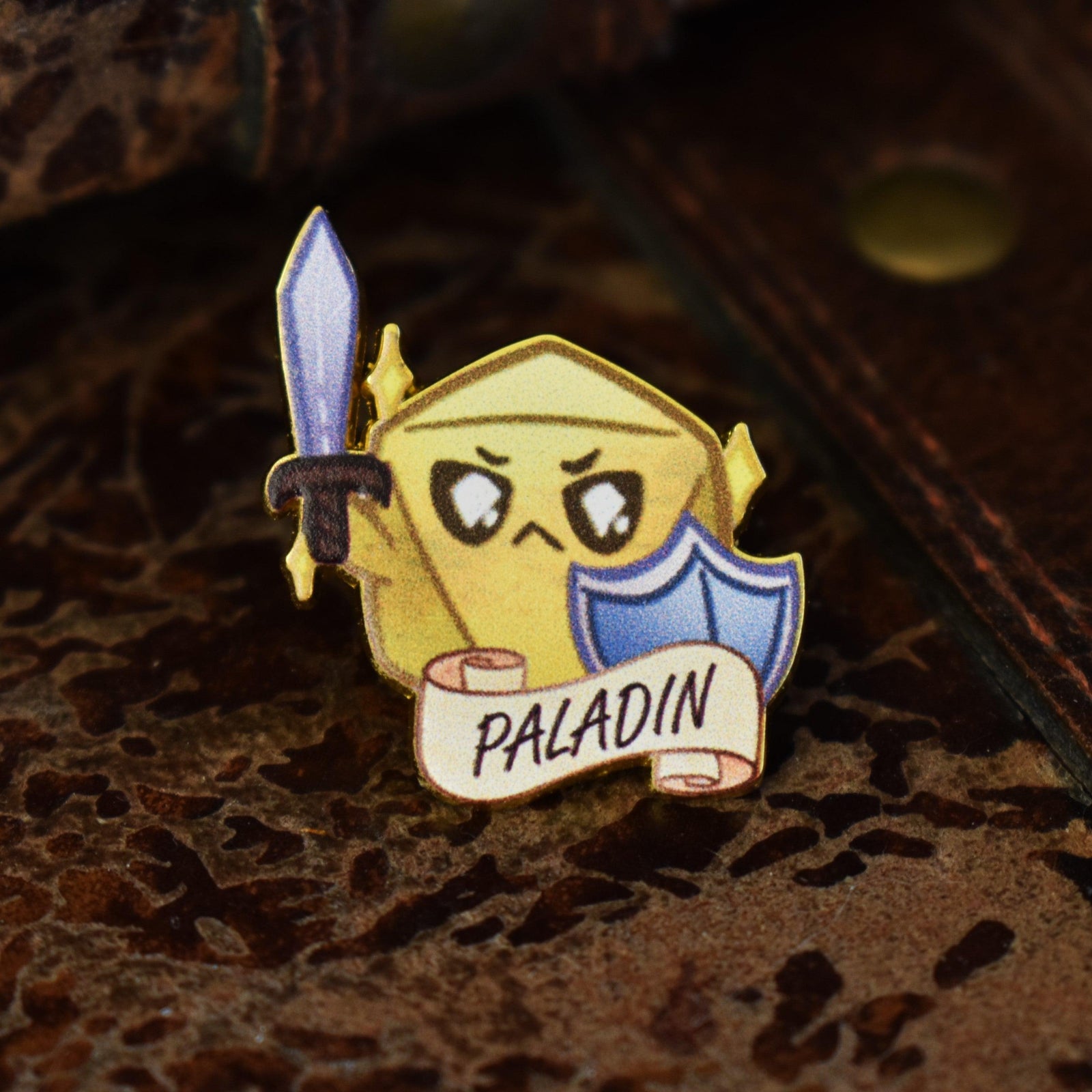 A colorful enamel pin featuring a paladin class character from D&D, with a sword and shield, displaying the word 'PALADIN' on a banner.
