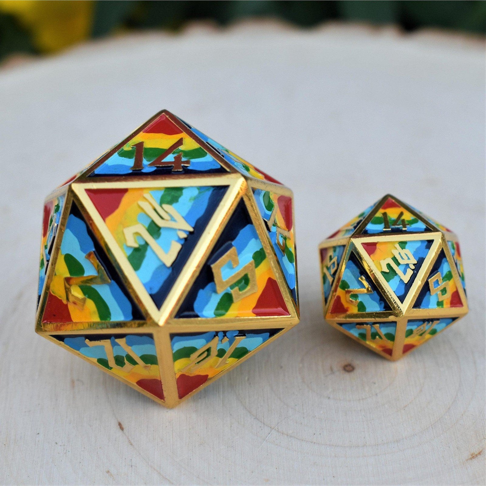 A set of colorful, embossed metal D20 dice with gold-colored edges, displayed on a wooden surface. The dice feature a nordic font and a rainbow-like pattern.