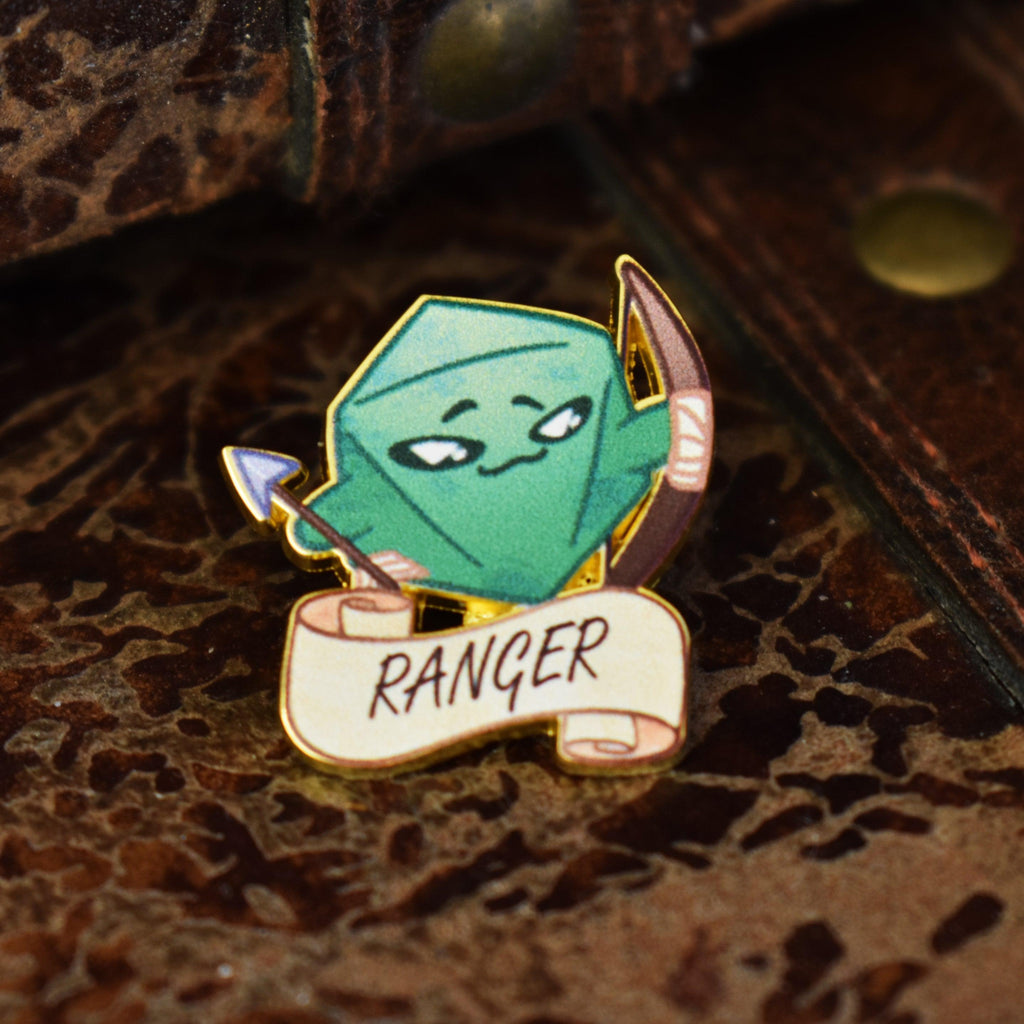 An enamel pin with a green, gold, and white color scheme featuring a ranger class character from a role-playing game, with the word 'RANGER' on a banner.