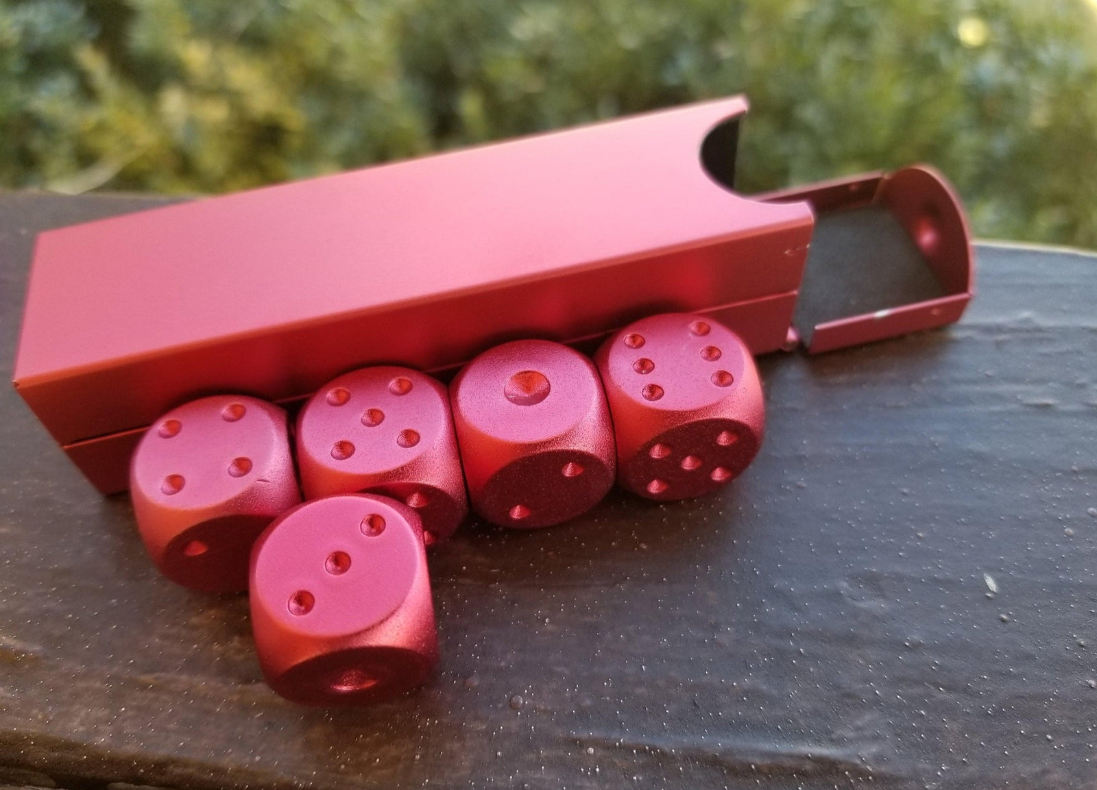 A set of red aluminum D6 dice with engraved numbers, displayed alongside a red foam-lined case.