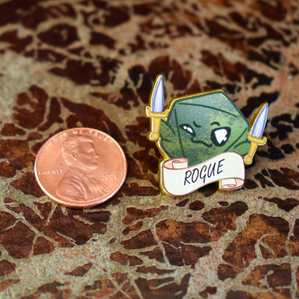 An enamel pin with a character illustration resembling a 'Rogue' class from D&D, featuring a green tone with a sword and the text 'ROGUE' on a banner.