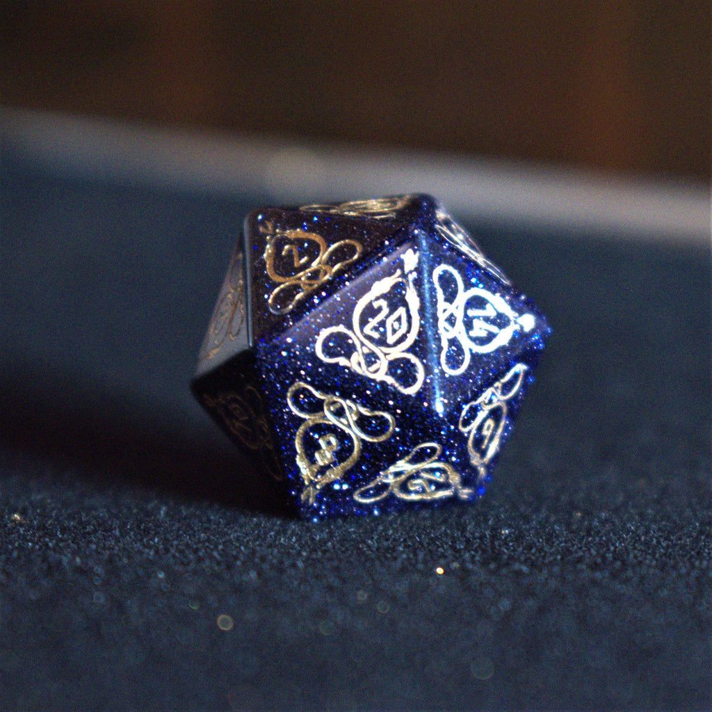 A close-up of hand-carved viking inspired blue sandstone ttrpg dice with engraved numbers and designs in gold