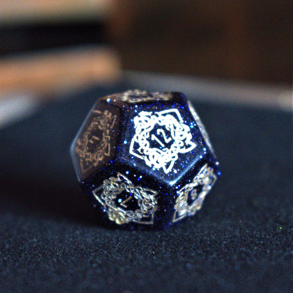 A close-up of hand-carved viking inspired blue sandstone ttrpg dice with engraved numbers and designs in gold