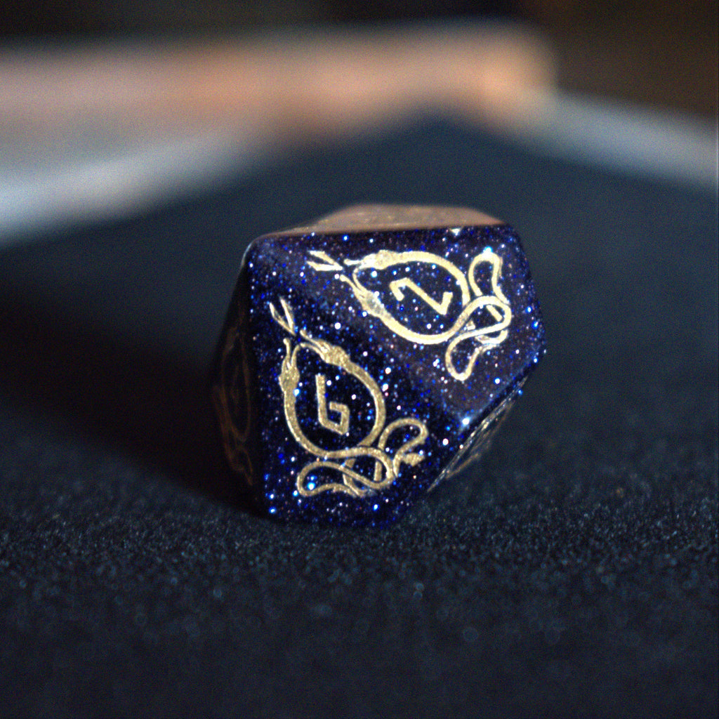 A close-up of hand-carved viking inspired blue sandstone ttrpg dice with engraved numbers and designs in gold