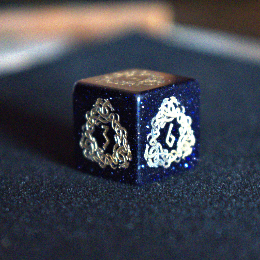 A close-up of hand-carved viking inspired blue sandstone ttrpg dice with engraved numbers and designs in gold