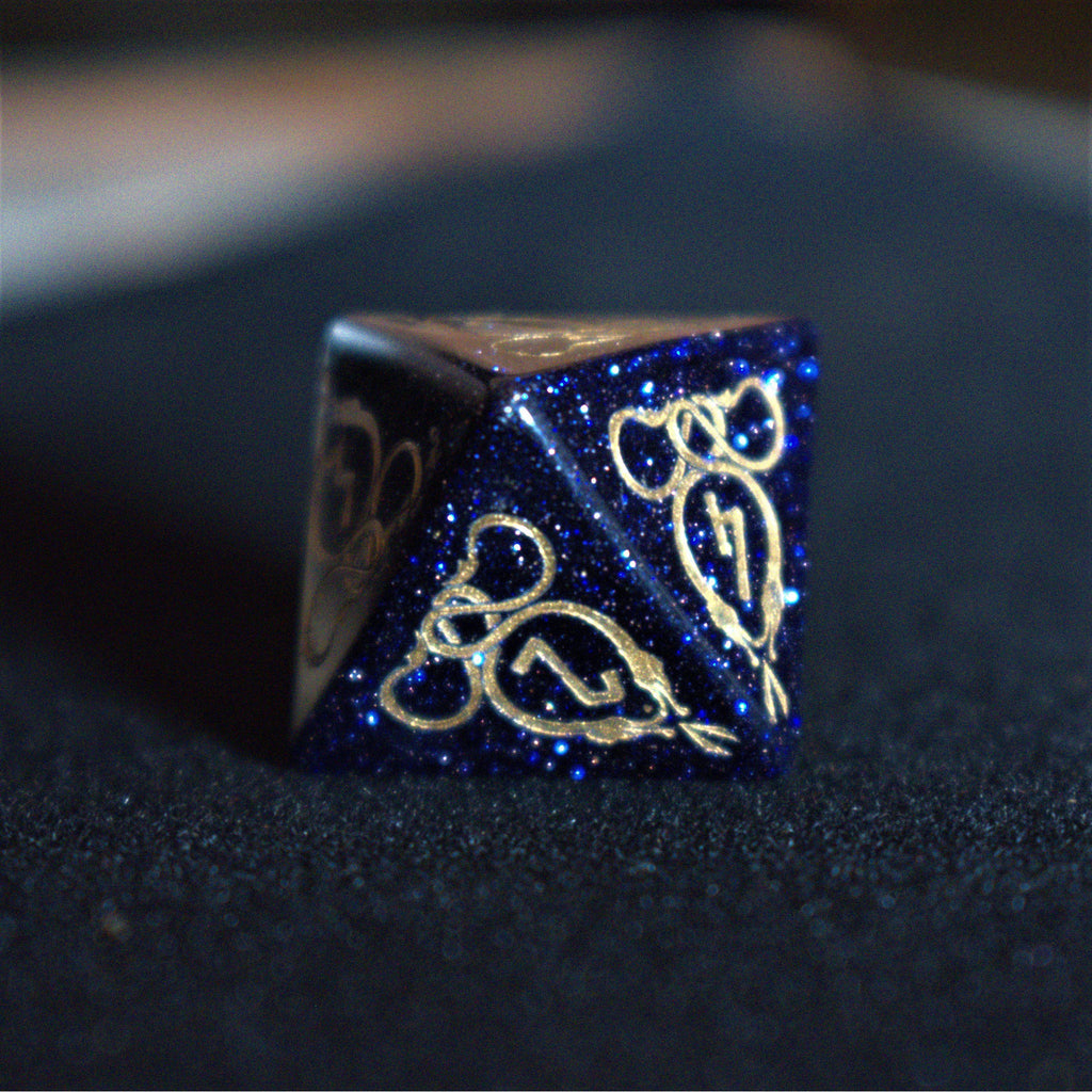 A close-up of hand-carved viking inspired blue sandstone ttrpg dice with engraved numbers and designs in gold