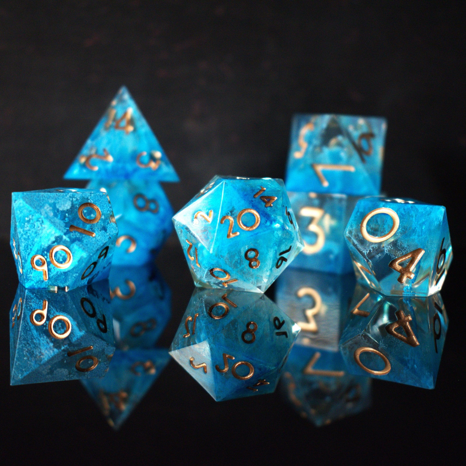 A set of sharp-edged resin dice in blue with gold numbers, including various shapes typical for RPG games.