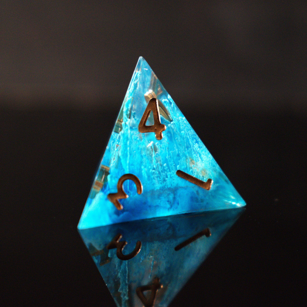 A set of sharp-edged resin dice in blue with gold numbers, including various shapes typical for RPG games.