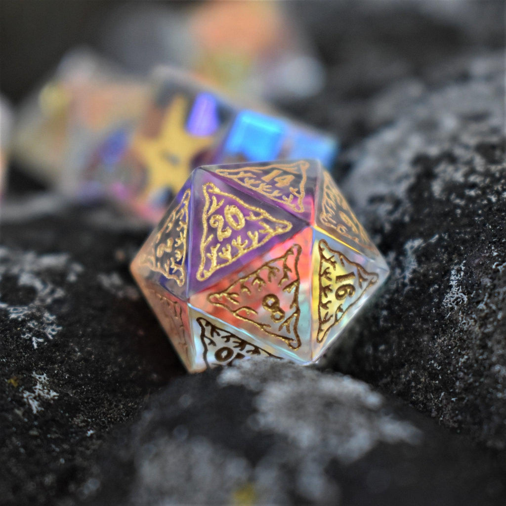 A set of hand-cut, multicolored prismatic glass polyhedral dice with engraved gold numbers and details inspired by the ocean on each face.