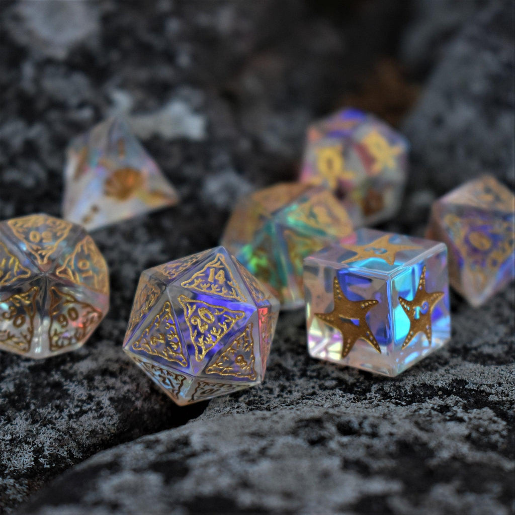 A set of hand-cut, multicolored prismatic glass polyhedral dice with engraved gold numbers and details inspired by the ocean on each face.
