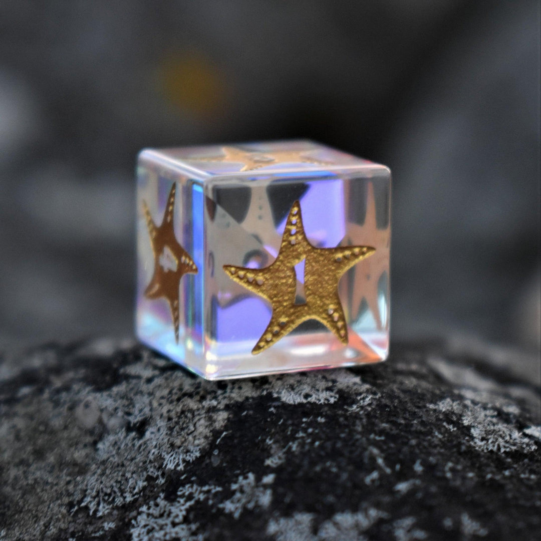 A set of hand-cut, multicolored prismatic glass polyhedral dice with engraved gold numbers and details inspired by the ocean on each face.