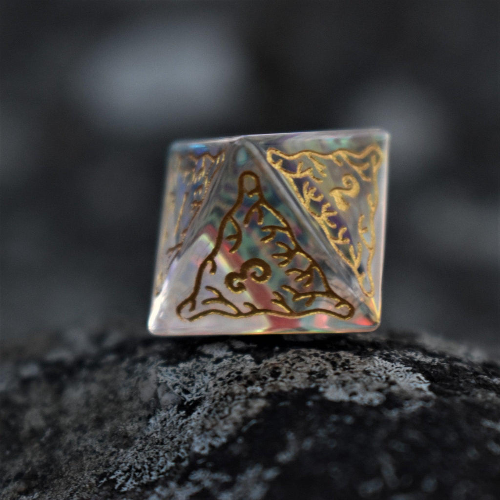 A set of hand-cut, multicolored prismatic glass polyhedral dice with engraved gold numbers and details inspired by the ocean on each face.