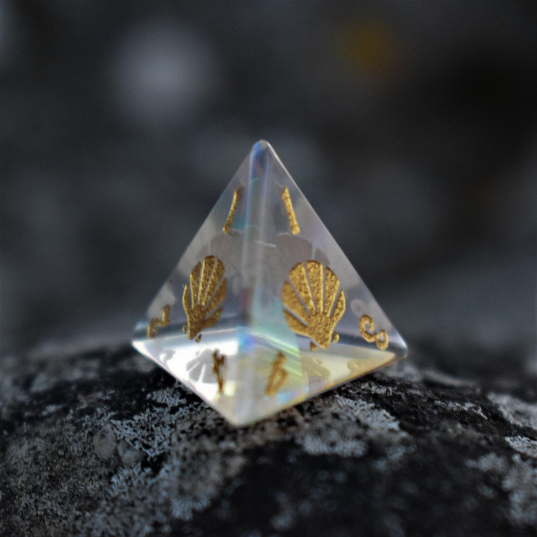 A set of hand-cut, multicolored prismatic glass polyhedral dice with engraved gold numbers and details inspired by the ocean on each face.