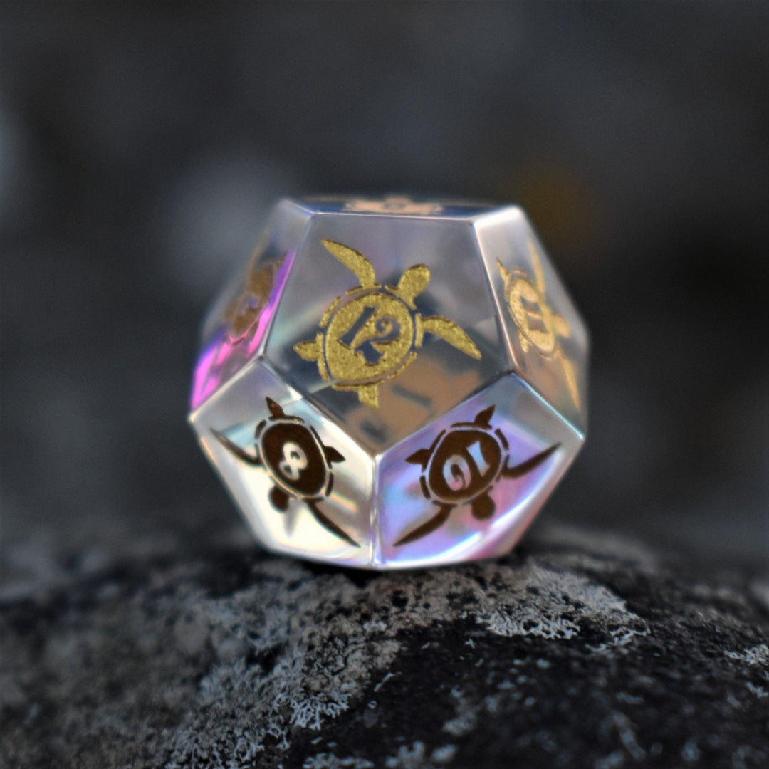 A set of hand-cut, multicolored prismatic glass polyhedral dice with engraved gold numbers and details inspired by the ocean on each face.