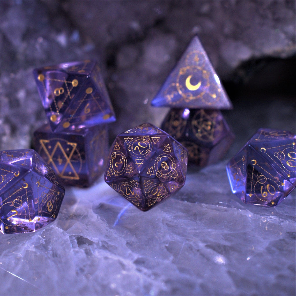 A set of purple glass dice with engraved golden numbering and details for tabletop gaming and collectors