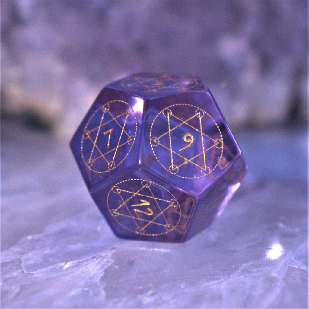 A set of purple glass dice with engraved golden numbering and details for tabletop gaming and collectors