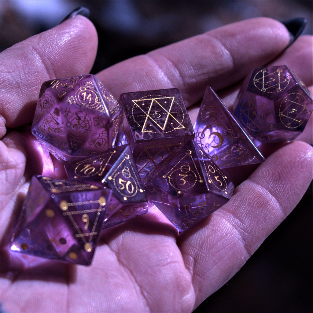 A set of purple glass dice with engraved golden numbering and details for tabletop gaming and collectors in a hand