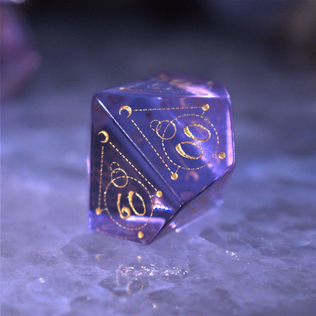 A set of purple glass dice with engraved golden numbering and details for tabletop gaming and collectors