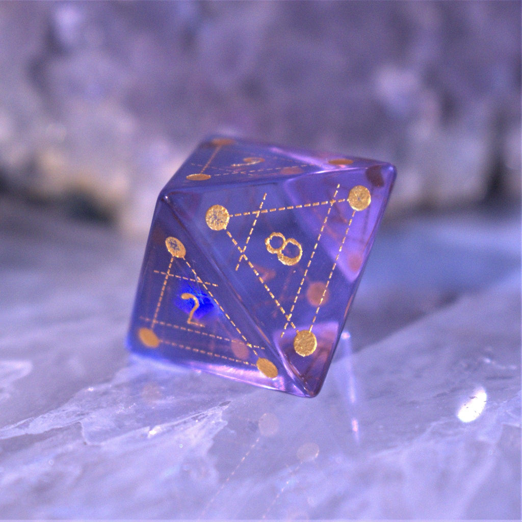 A set of purple glass dice with engraved golden numbering and details for tabletop gaming and collectors