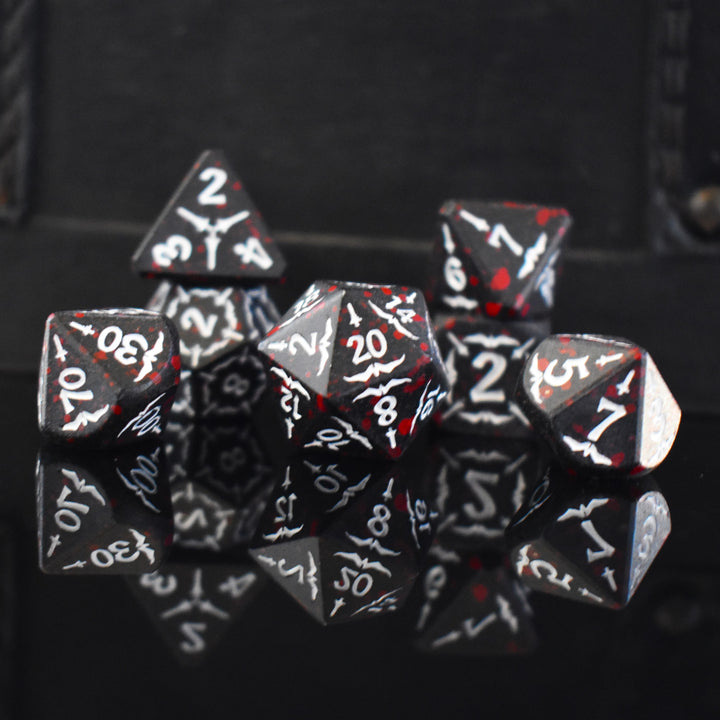A set of black metal polyhedral dice with blood splatter across them and white numbering and sword details for tabletop gaming and board games