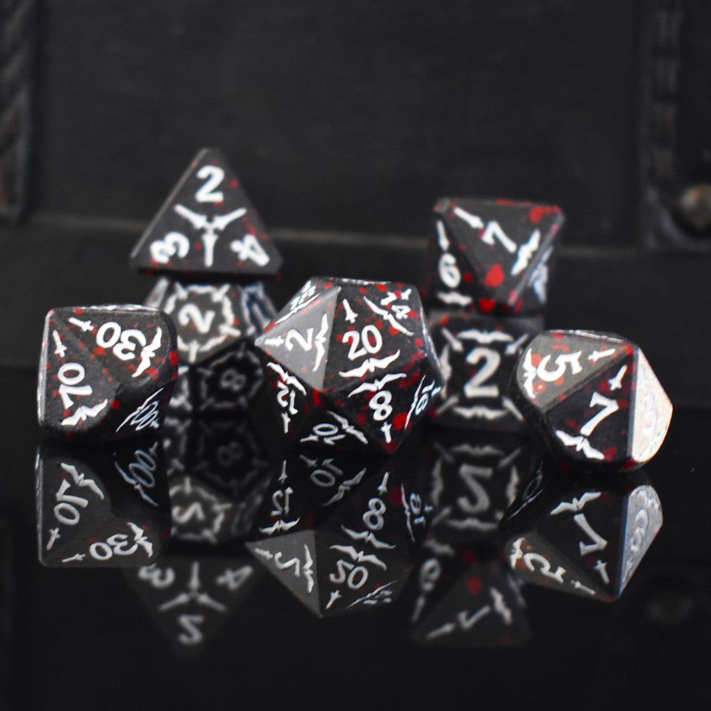 A set of black metal polyhedral dice with blood splatter across them and white numbering and sword details for tabletop gaming and board games