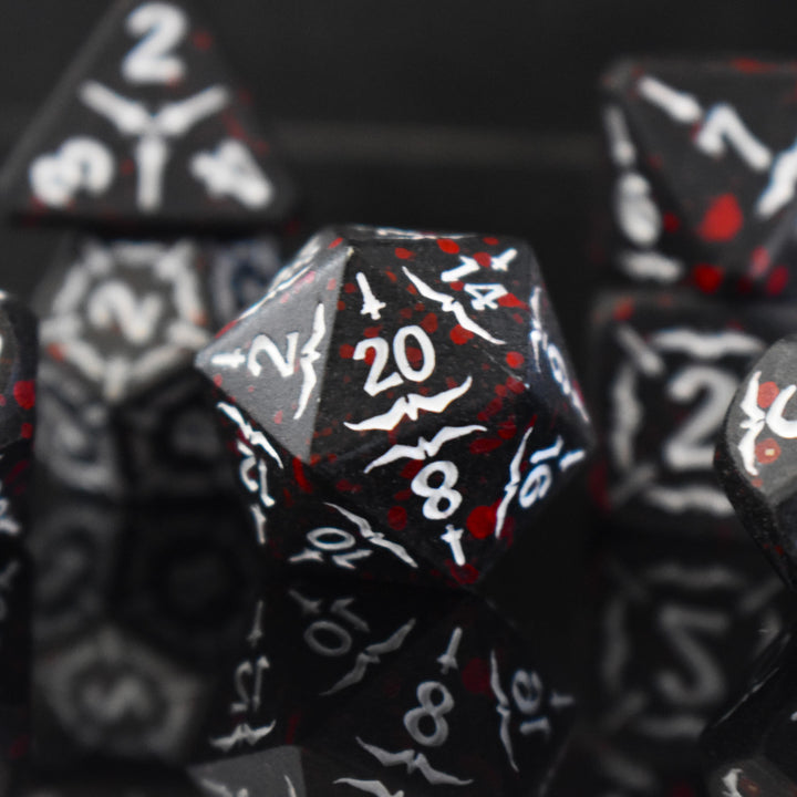 A set of black metal polyhedral dice with blood splatter across them and white numbering and sword details for tabletop gaming and board games