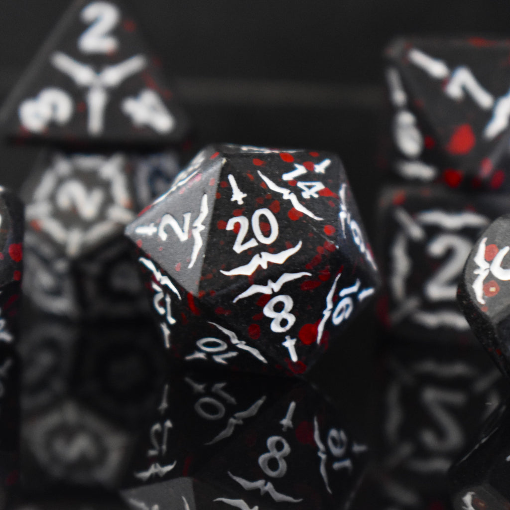 A set of black metal polyhedral dice with blood splatter across them and white numbering and sword details for tabletop gaming and board games
