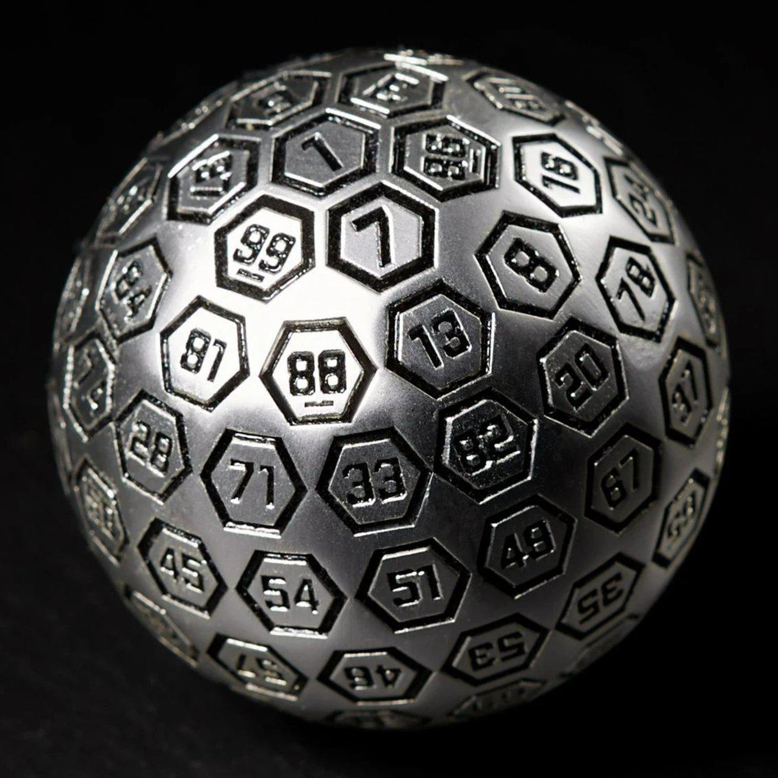 A large, silver, metal D100 dice with black engravings on a hexagonal pattern.